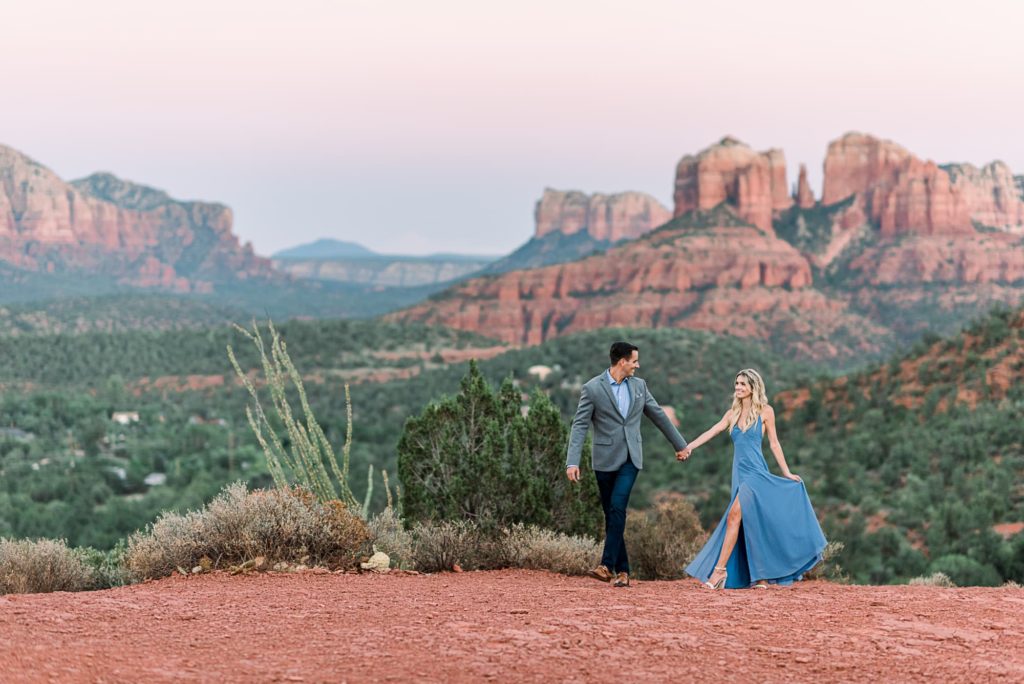 Engagement photo of couple walking with Cathedral Rock in the background