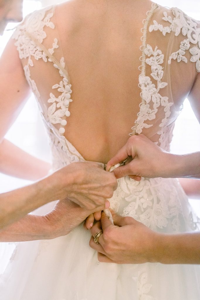 Bride with mother and maid of honor doing up the back of her dress