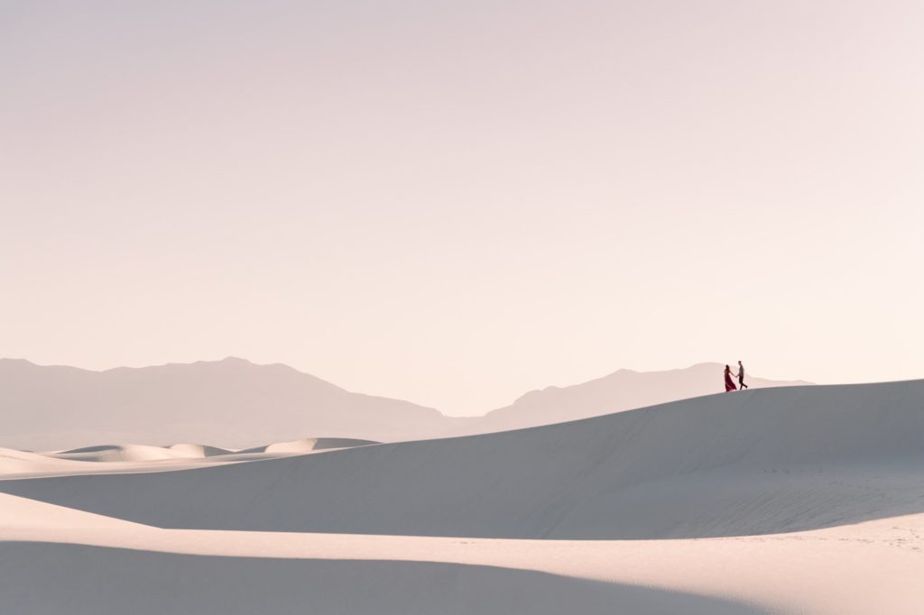 Couple walking in the distance at White Sands New Mexico with beautiful white sand dunes around them.
