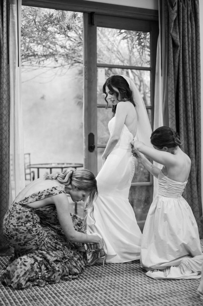 Bride putting on wedding dress and bridesmaid putting on brides shoes