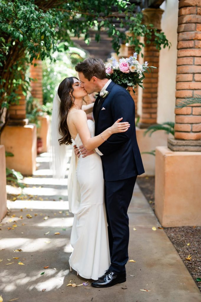 bride and groom kissing in an outdoor corridor lined with pillars at Royal Palms