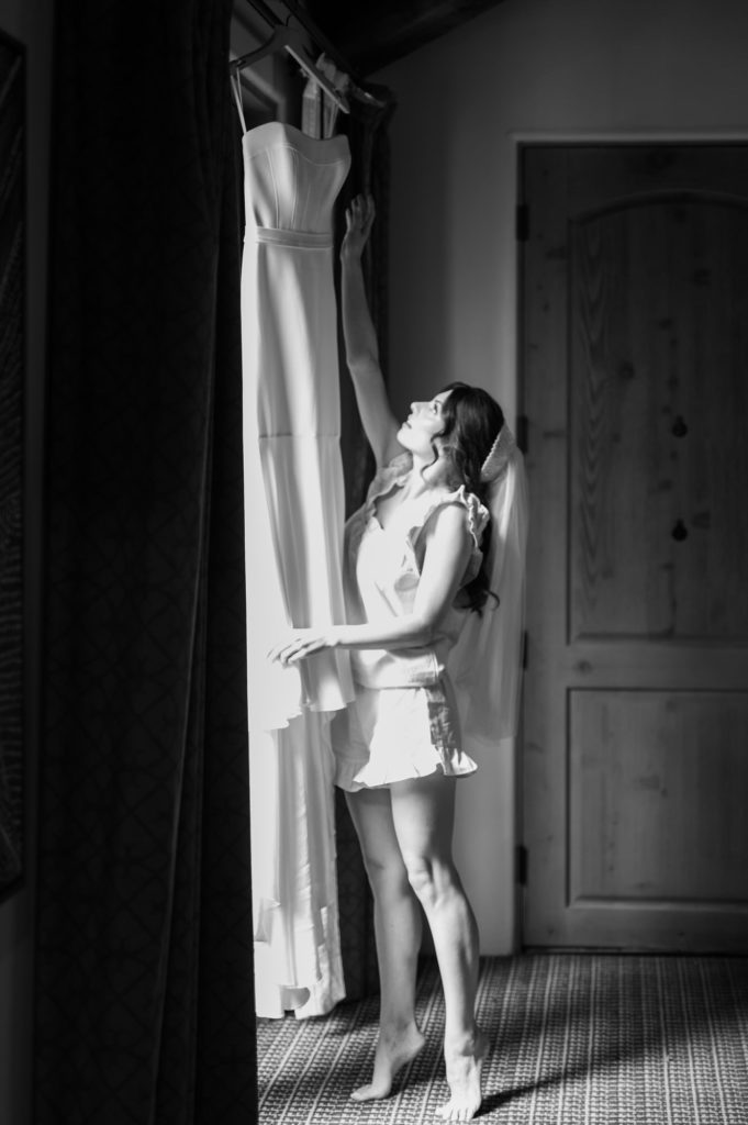 Bride taking wedding dress of the hanger in front of a window