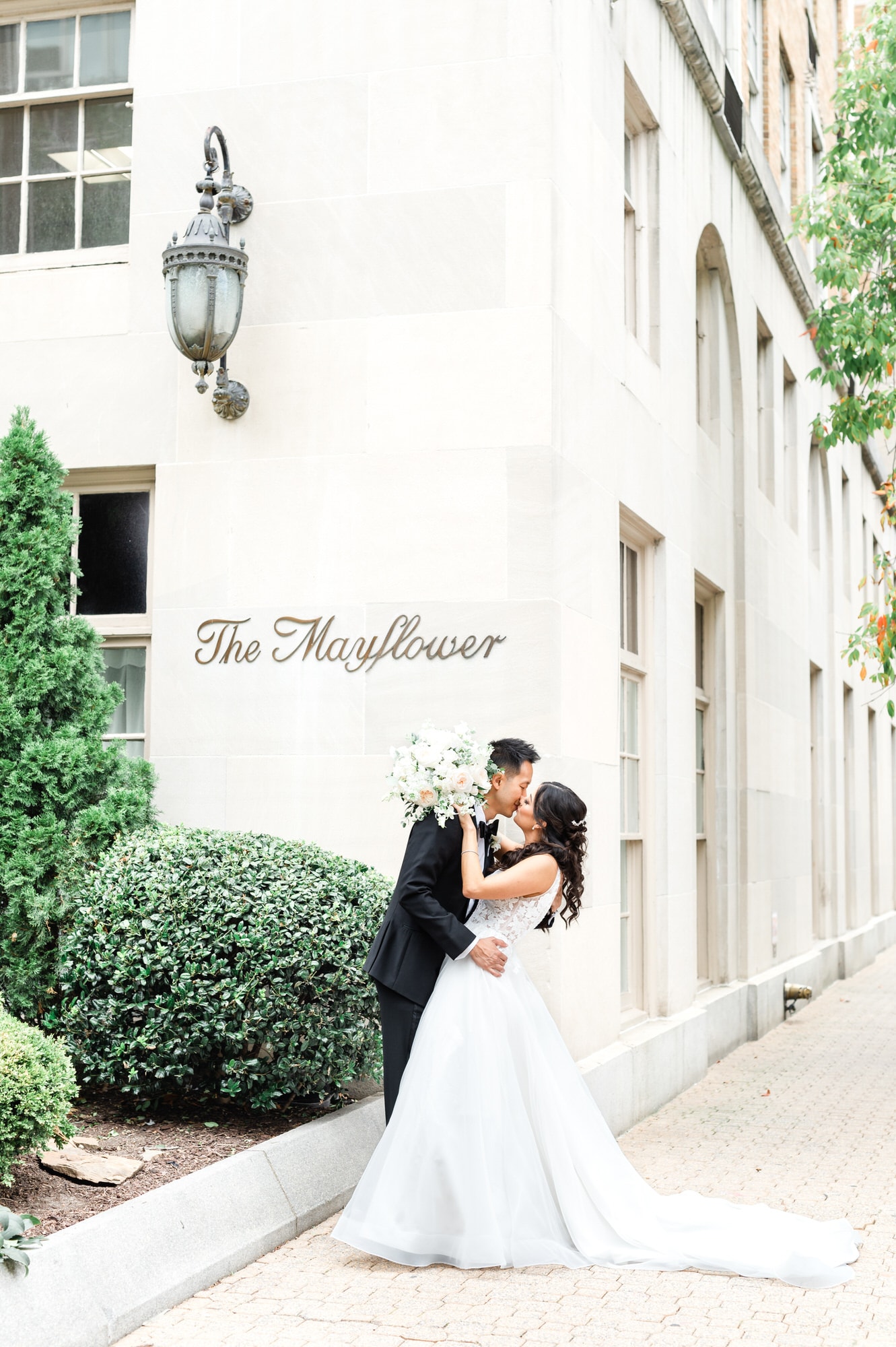 Mayflower Hotel DC Wedding couple standing outside on sidewalk kissing with the Mayflower sign on the building in the background