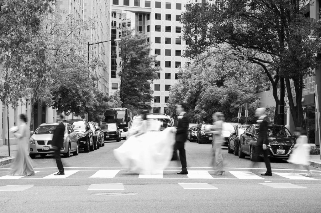 Bridal party with a slight motion blur crossing the street with the Mayflower Wedding Venue behind them