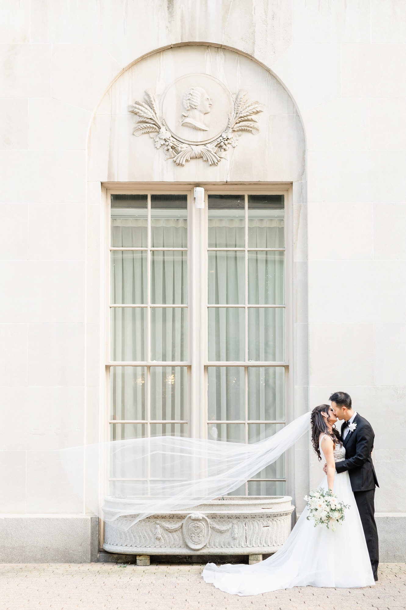 Bride and Groom kissing on the sidewalk in front of a tall large window at The Mayflower Hotel DC