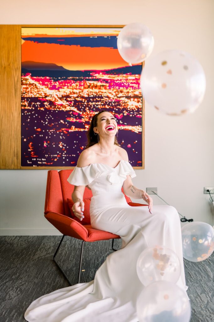 Bride sitting in a chair laughing as she bounces up balloons.