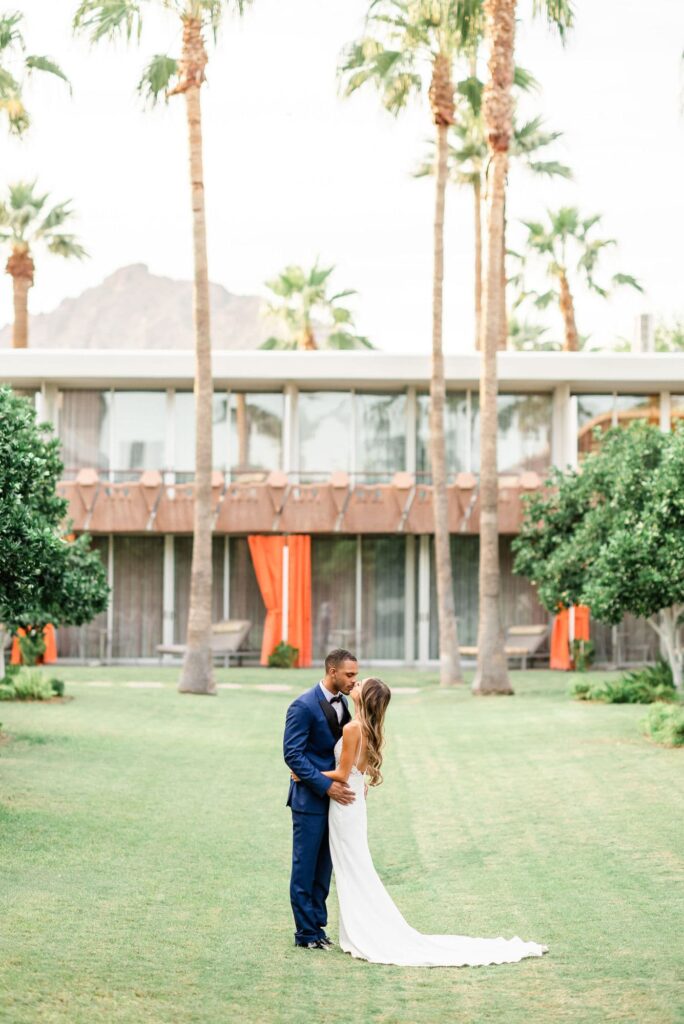 Bride and groom kissing on the lawn in front of Hotel Valley Ho with palm trees and mountains in the background